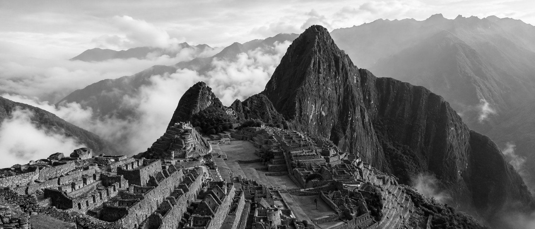 Vista panorámica de Machu Picchu entre montañas y nubes al amanecer, en blanco y negro
