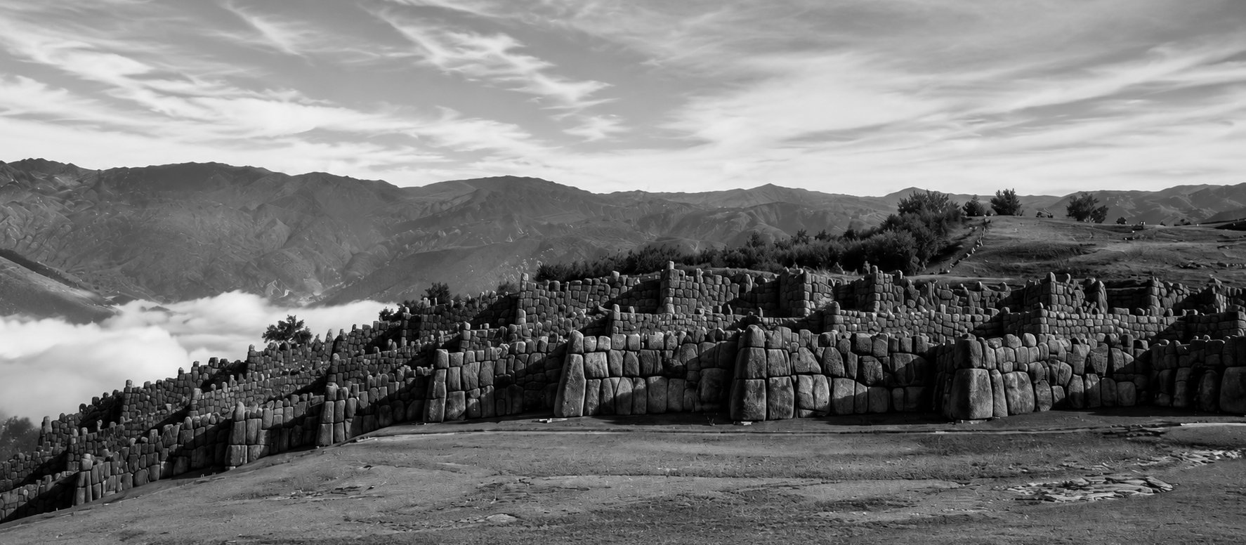Muros de piedra de la fortaleza inca de Sacsayhuamán bajo un cielo nublado, en blanco y negro, Cusco, Perú